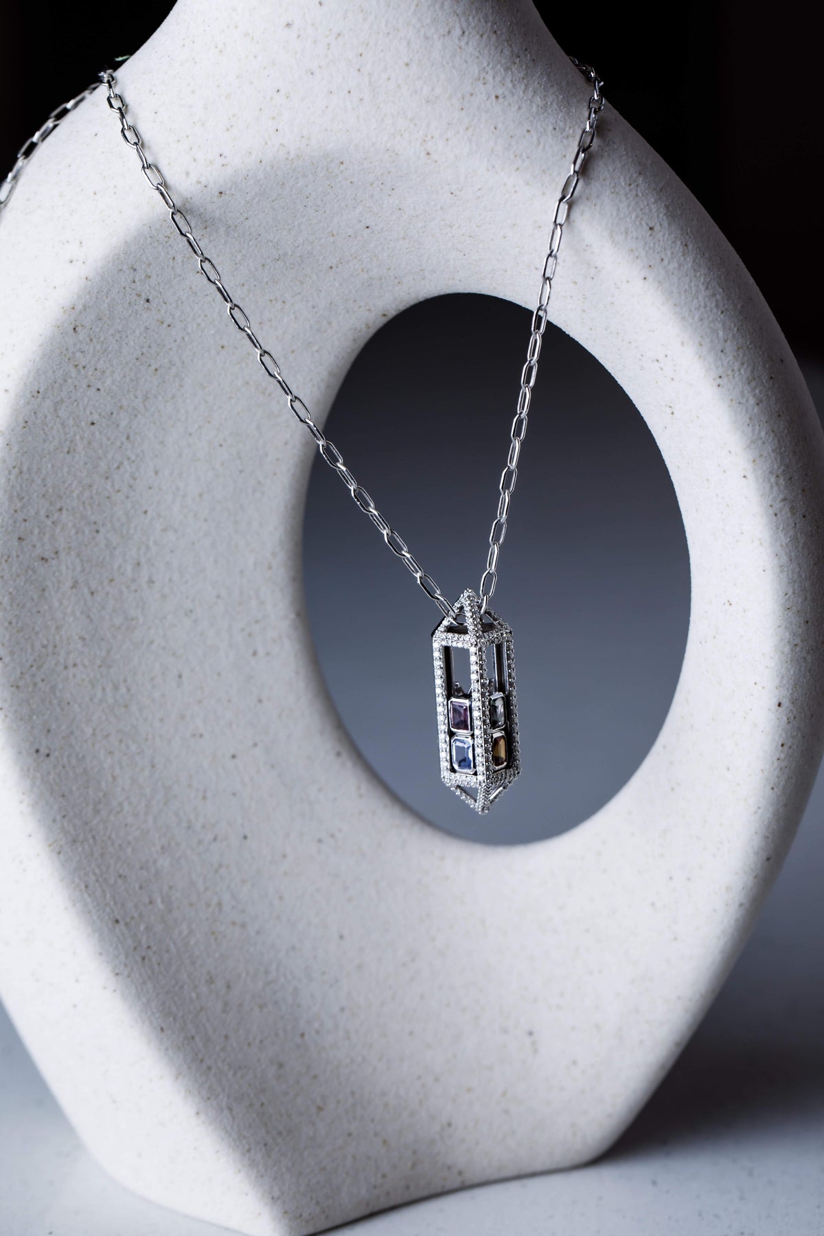 A diamond pendant necklace on a white sculpted stand