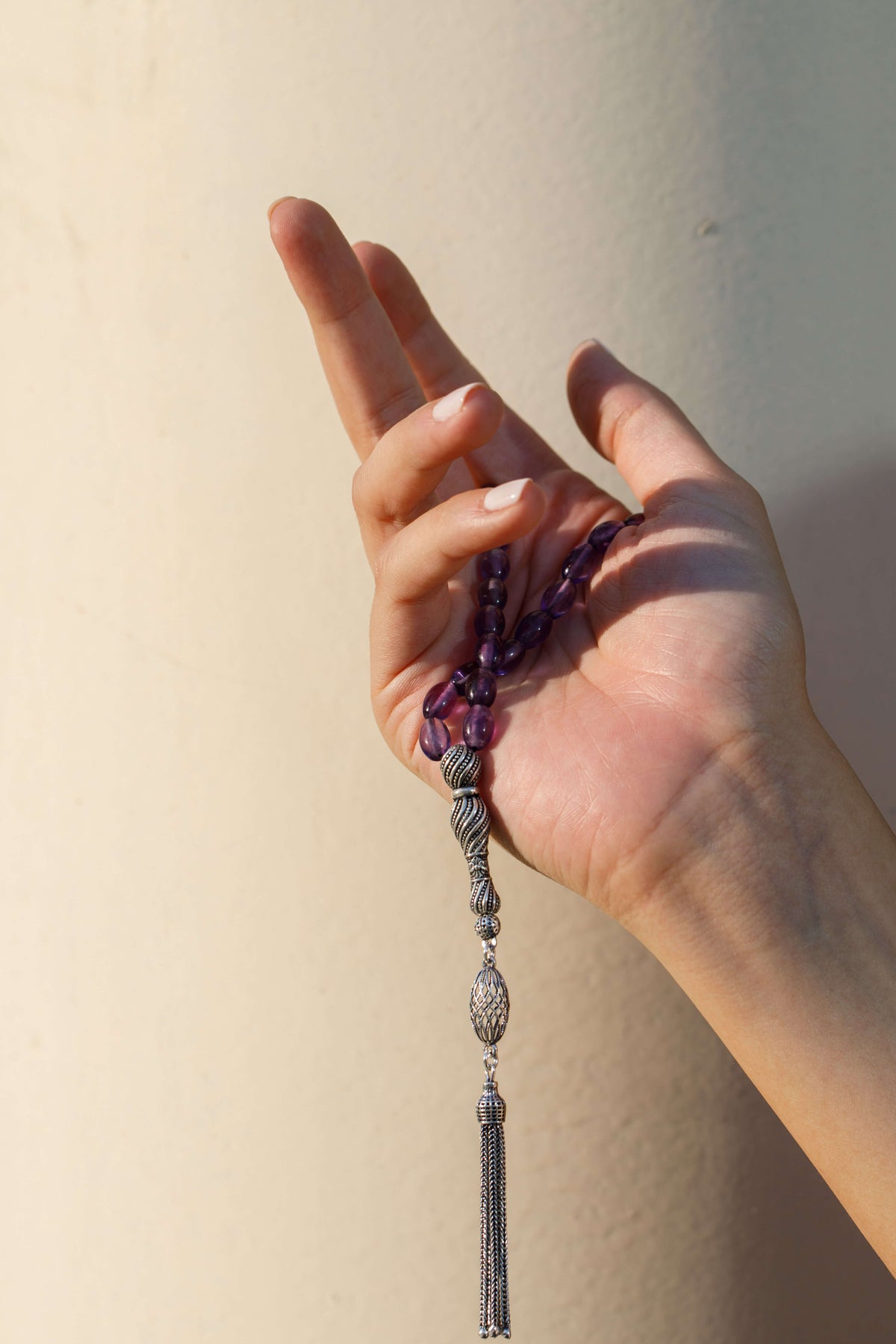 A hand holding a string of gemstone beads against pale stone